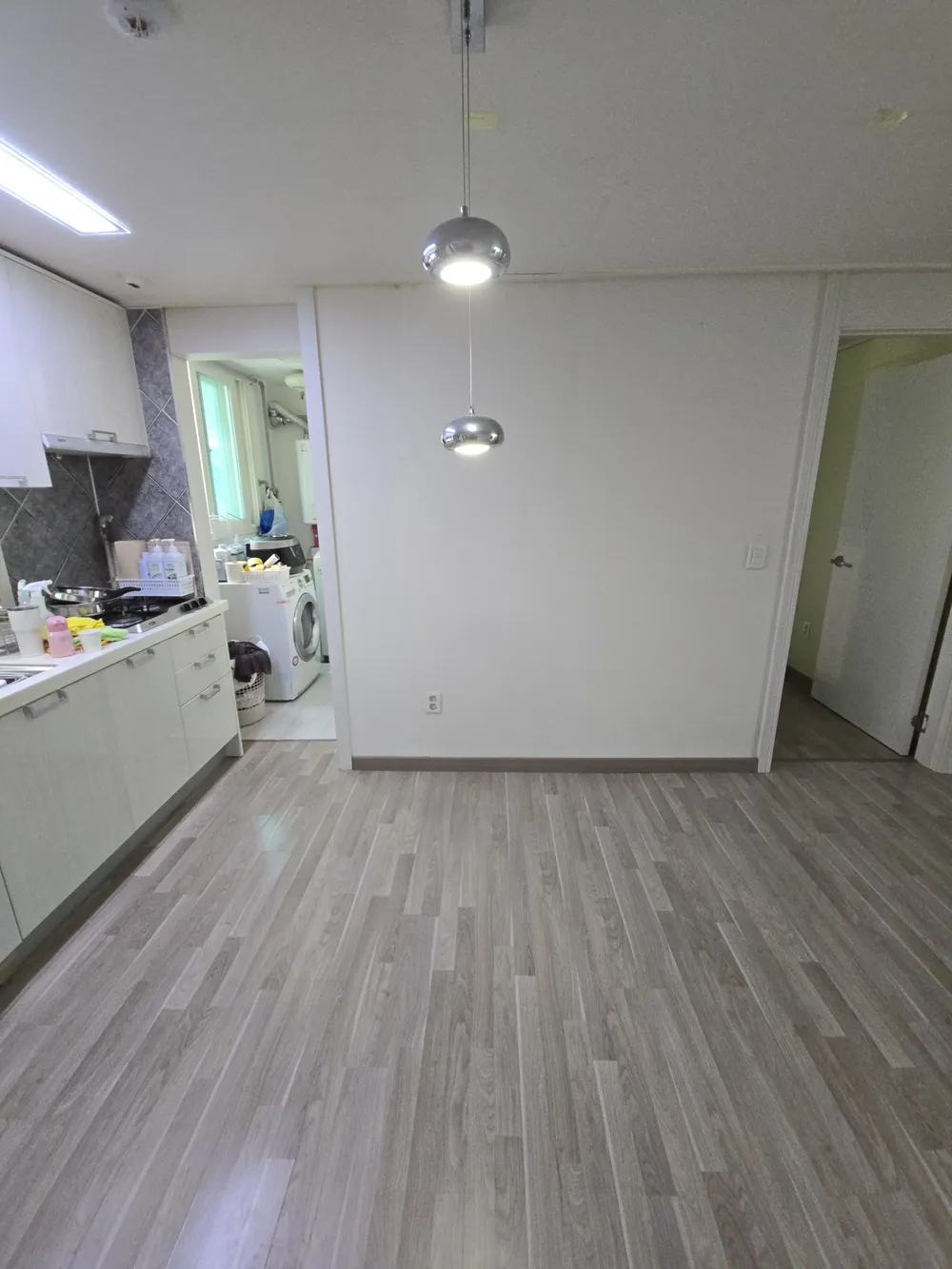 아일랜드가 없고 바닥이 넓게 보이며 벽과 펜던트 조명, 싱크 쪽 하부장이 보이는 주방